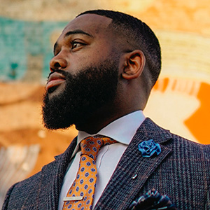 A man in a gray striped suit and orange tie is seen in front of a colorful orange and blue abstract background