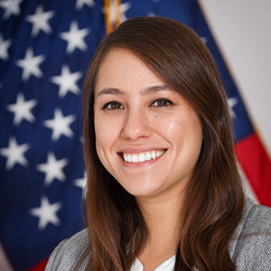 A woman in a gray suit jacket is seen in front of an American flag