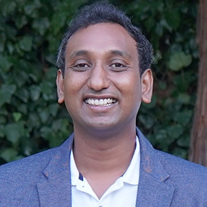 A man in a blue suit coat is seen in front of a wall of ivy