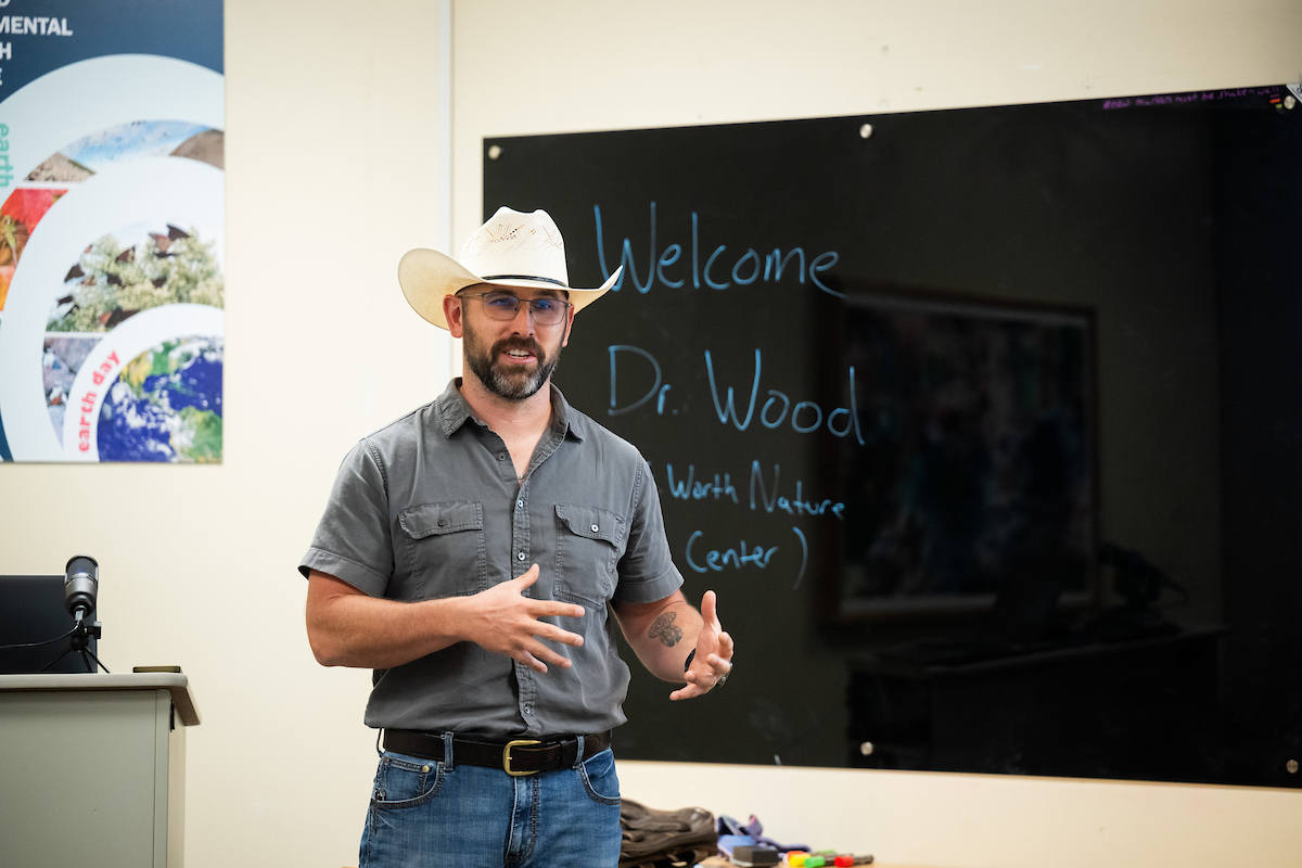 A man, Jared Wood, stands in front of a blackboard that says "Welcome Dr. Wood (Fort Worth Nature Center)