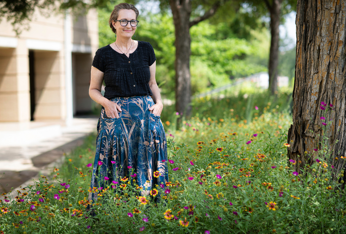 Jaime Baxter-Slye stands among native wildflowers. She wears a black button down and blue floral skirt.