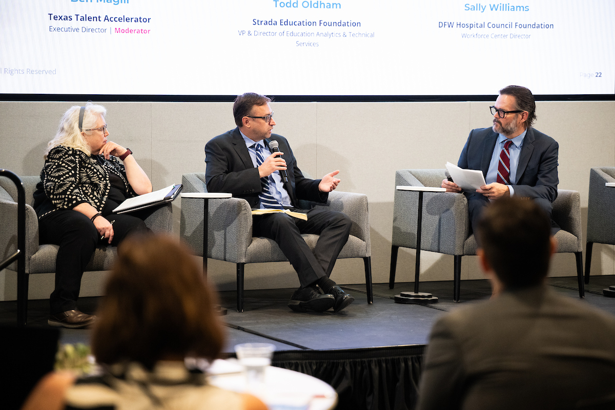 A woman and two men sit in chairs during a panel discussion