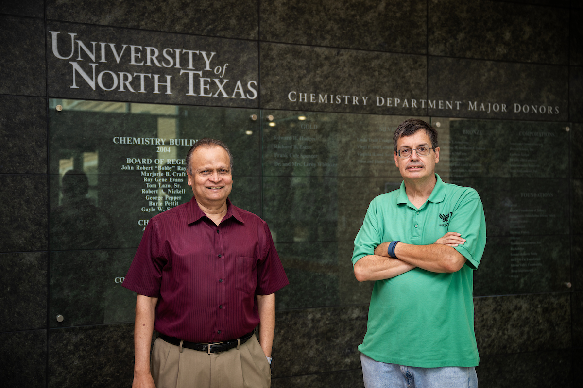 Regents Professors Francis D'Souza and Thomas Cundari stand next to each other in front of a marble wall that says University of North Texas