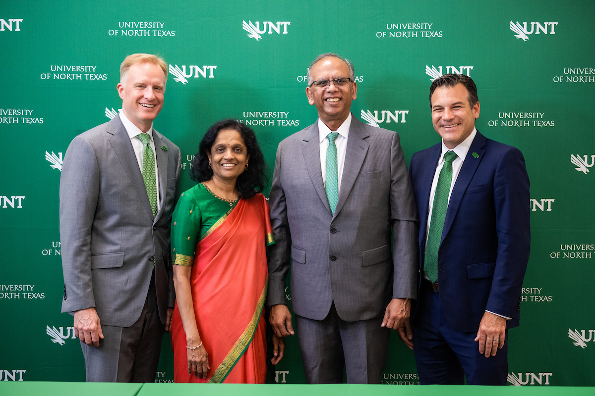 A man, a woman, then two men stand in a line in front of a UNT backdrop.