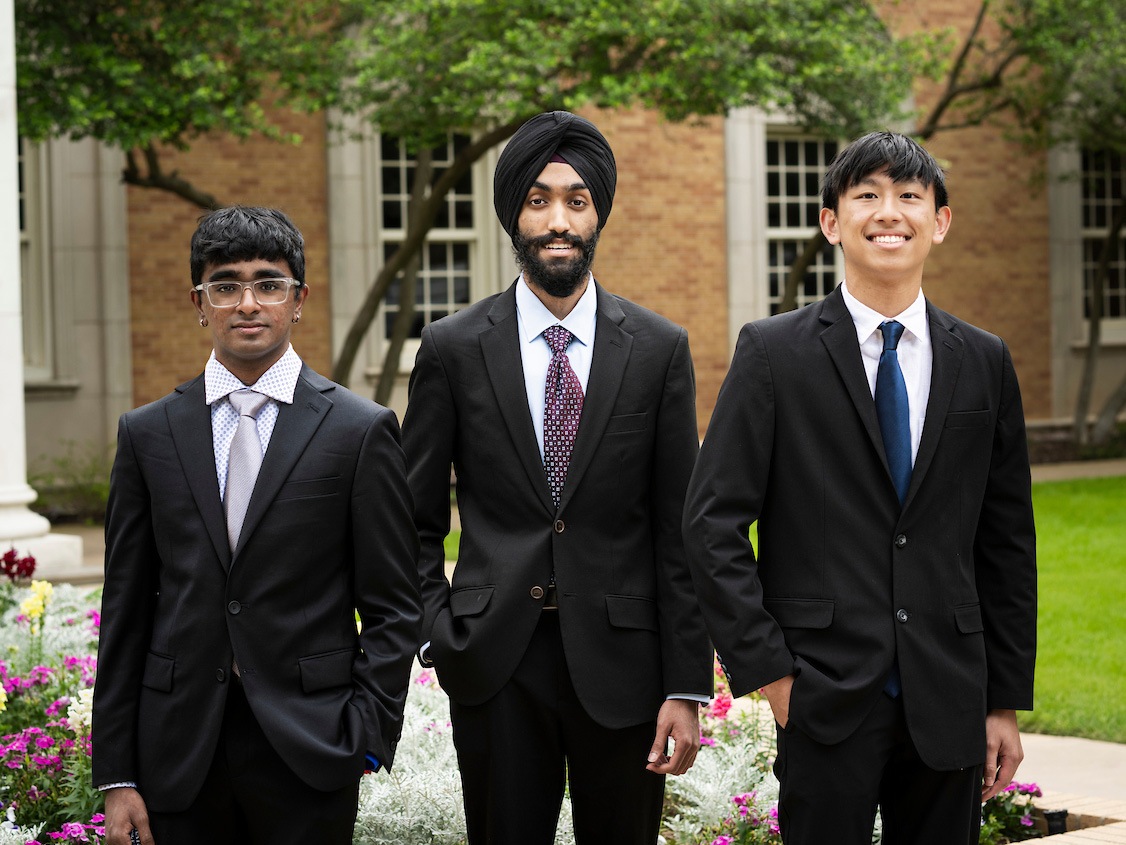 Aniruth Ananthanarayanan, Pavan Ahluwalia and Bradley Lin stand in a line wearing suits smiling at the camera.