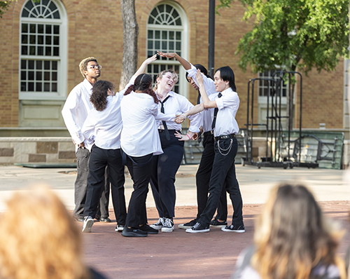 A group of dancers in black and white form a circle at the UNT Library Mall