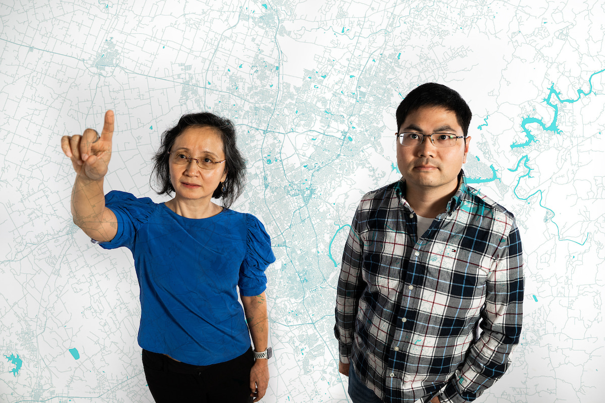 Yan Huang and Heng Fan stand side by side in front of a while wall, a blue map of roadways is overlayed on the photo