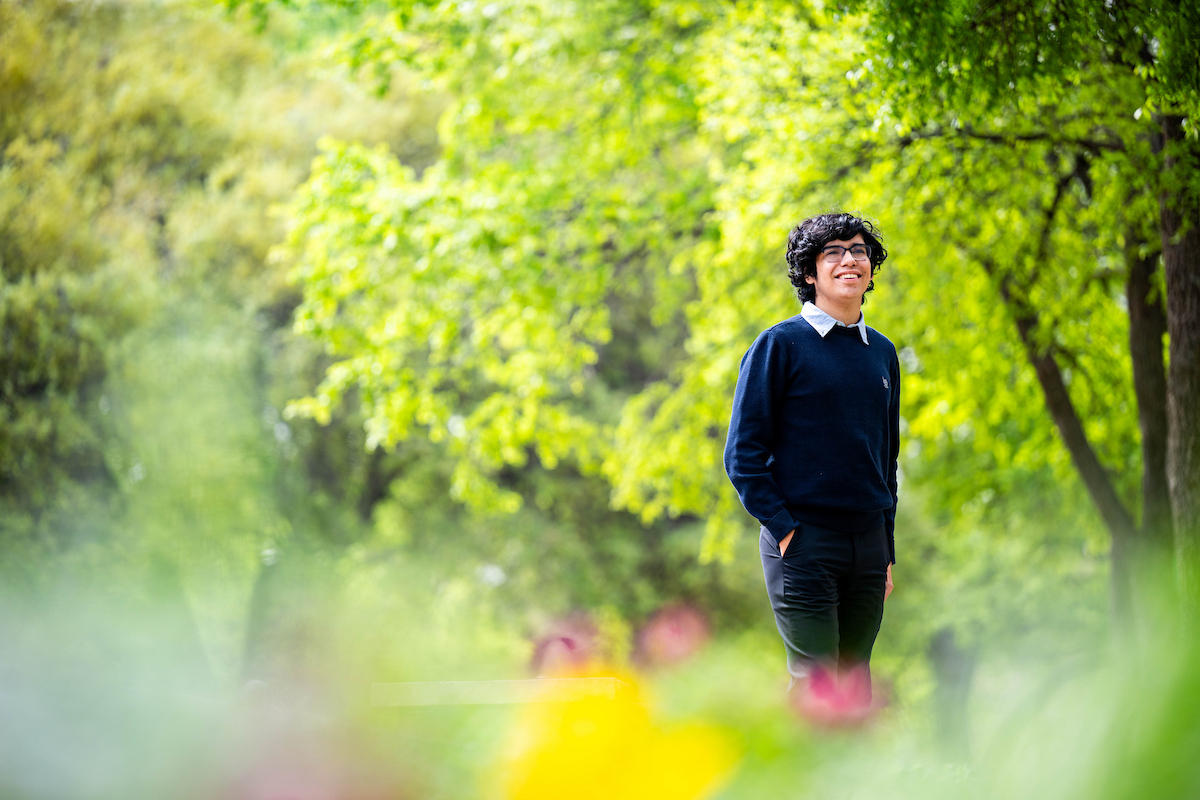 Alejandro Perez stands among green trees and flowers