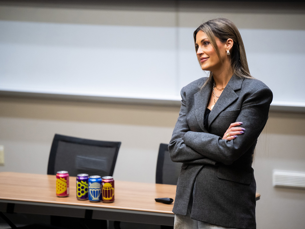 Allison Ellsworth looks out of frame with a smile on her face. She stands in front of a table with cans of the drink poppi on it 