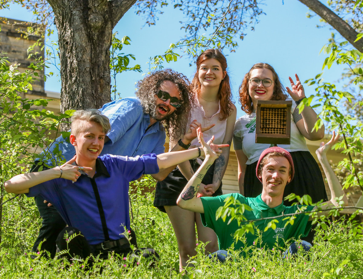 People outside posing for a photo with bee boxes