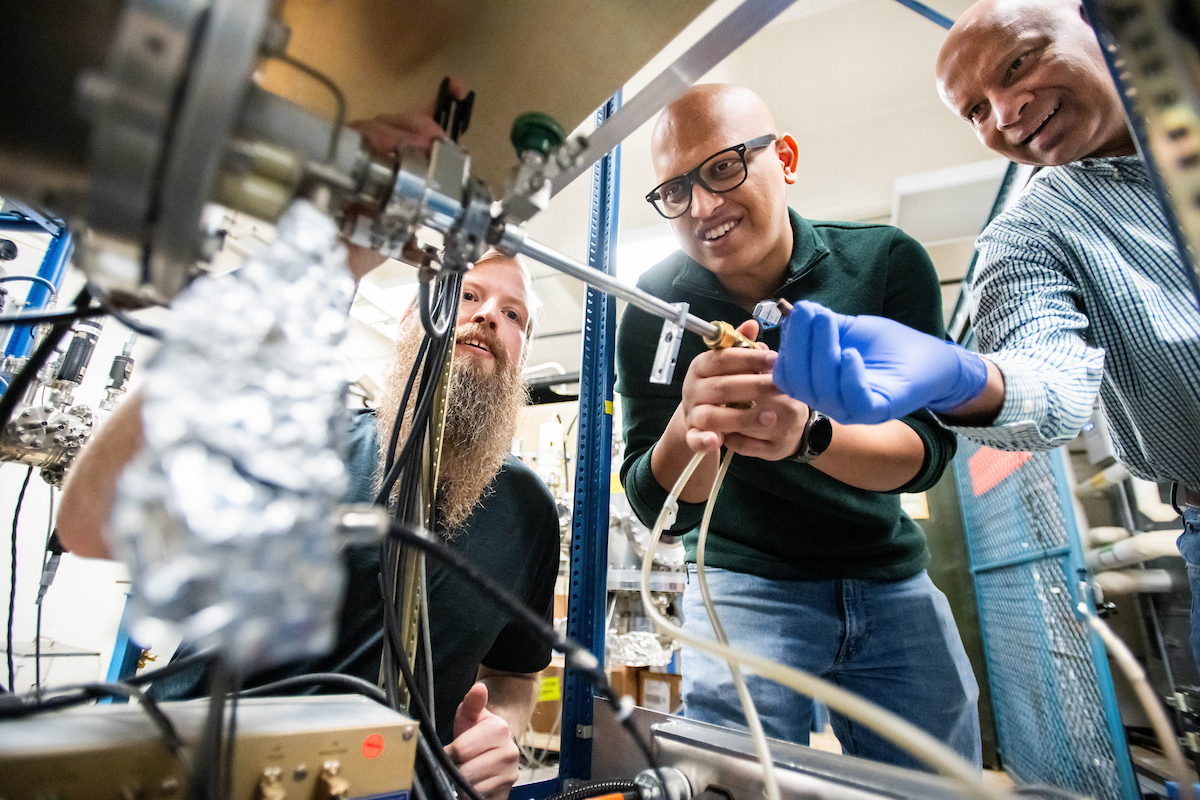 A lower angle shot up at three mean who are staring at machinery on a shelf.