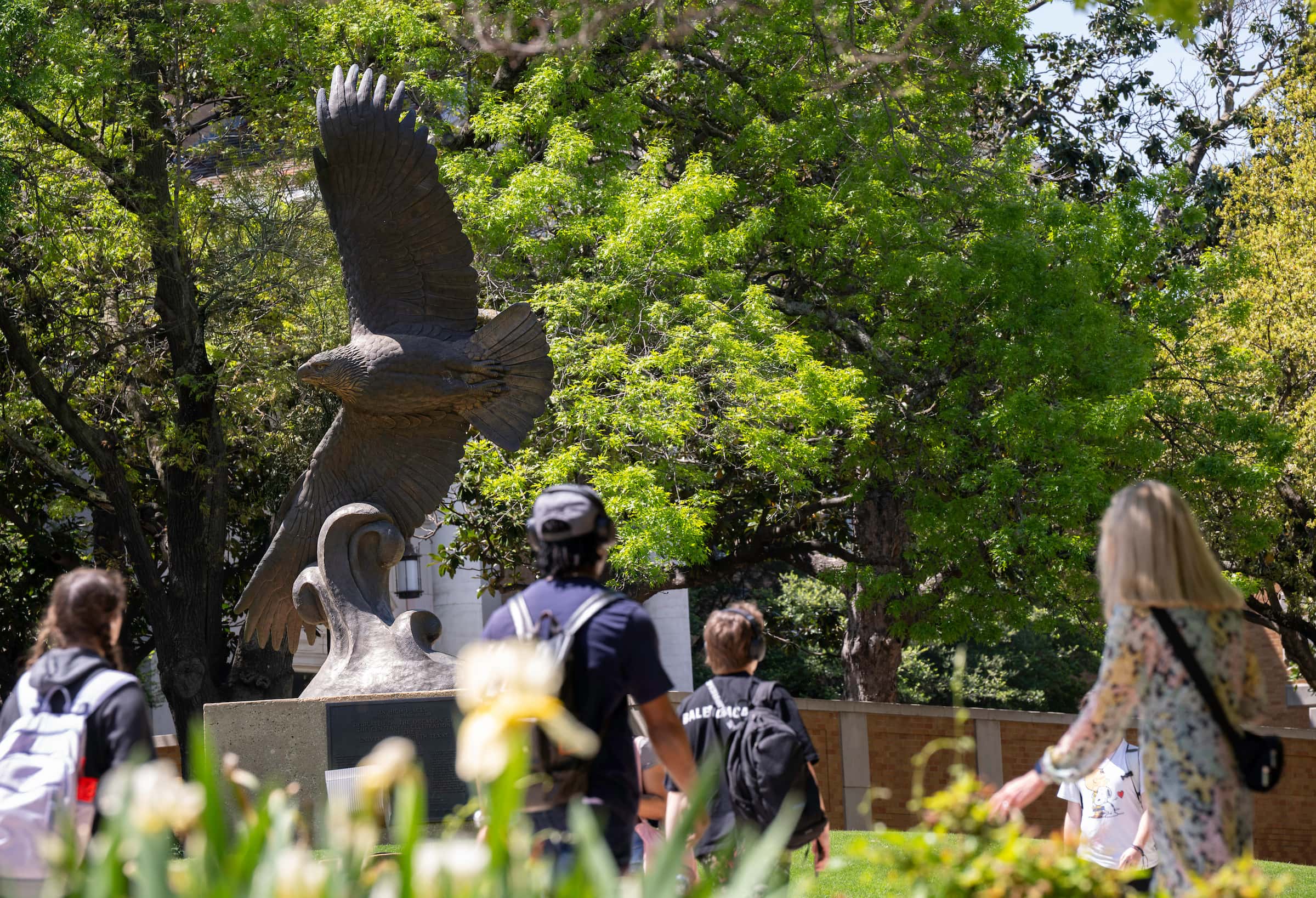 students walk outside in front of a bronze eagle statue