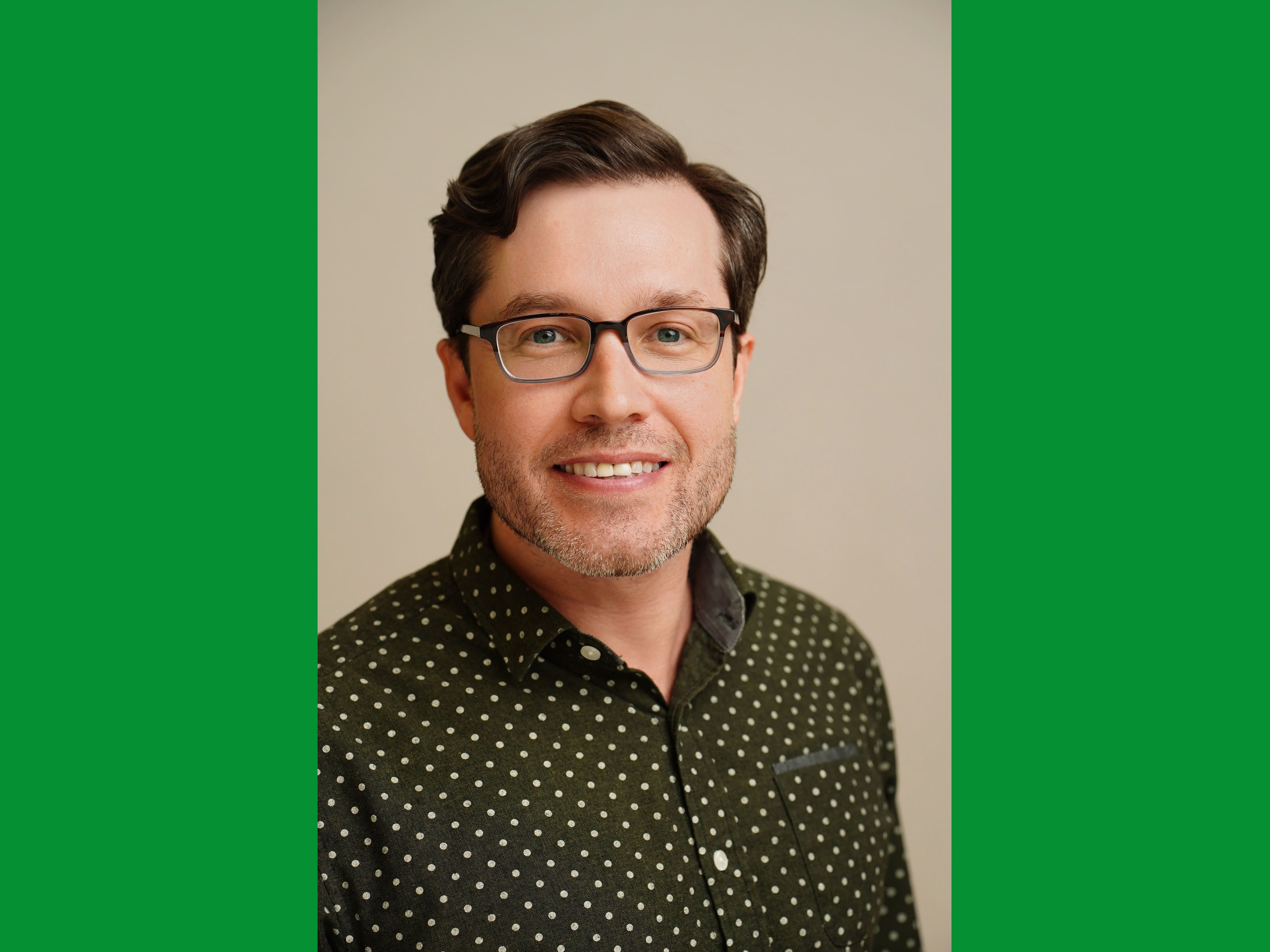 A headshot photo of Eric Dafoe wearing a black polka dot button down. There are green bars on the side of he photo to make it fit a 4x3 rectangle.