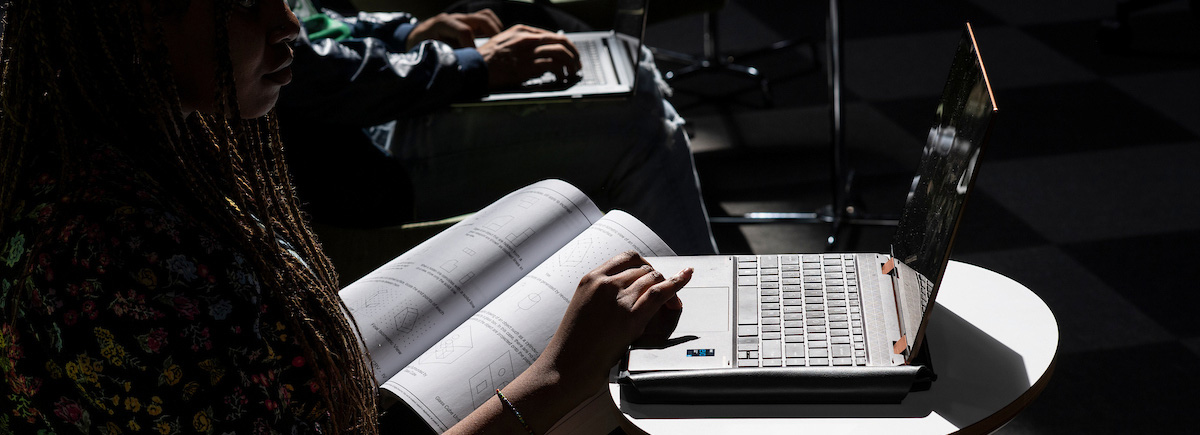 A laptop is highlighted by a sun beam while a student in shadow uses it
