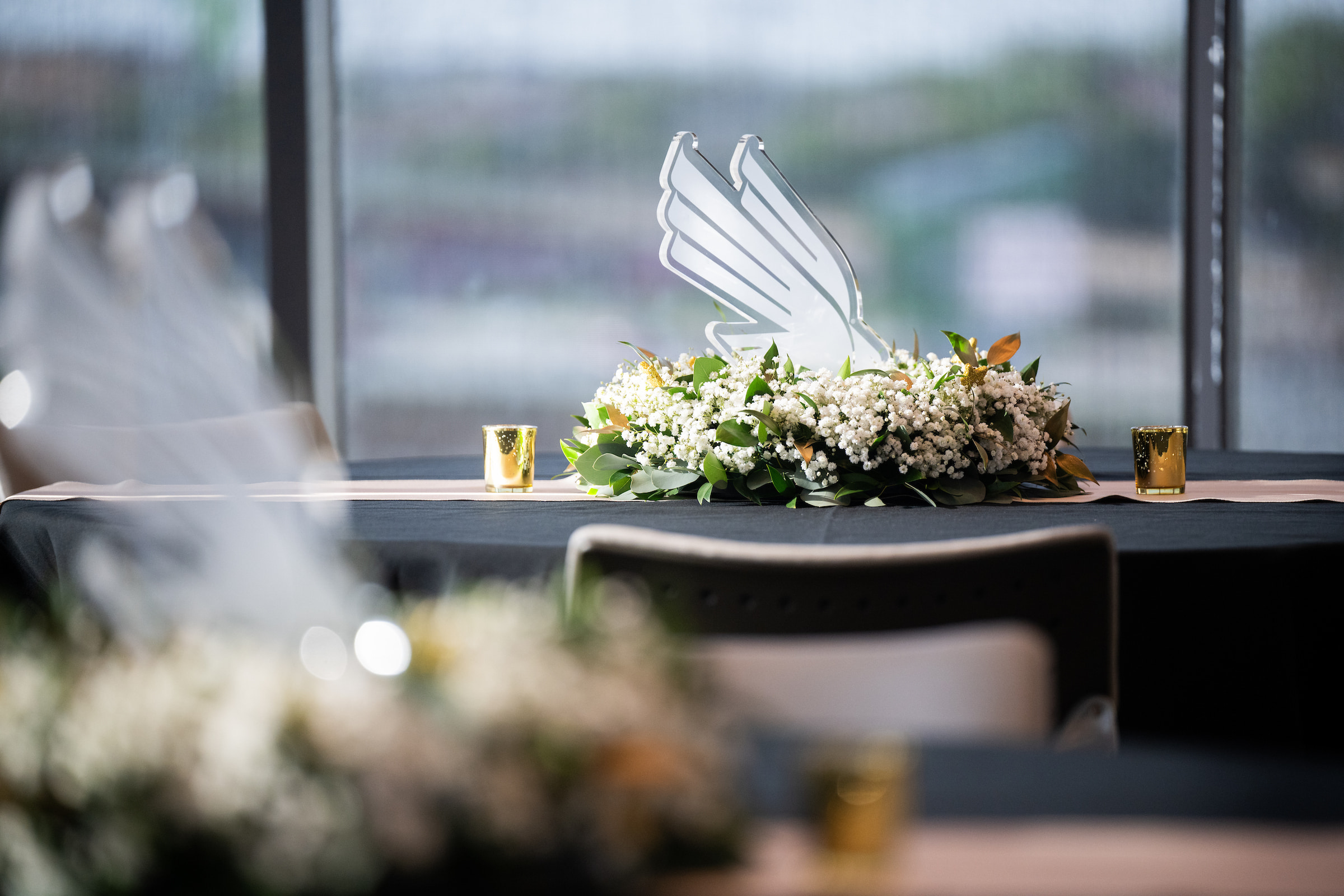 An award in the shape of UNT's stylized diving eagle sits on a table within a flower ring. Two candles flank the flowers.