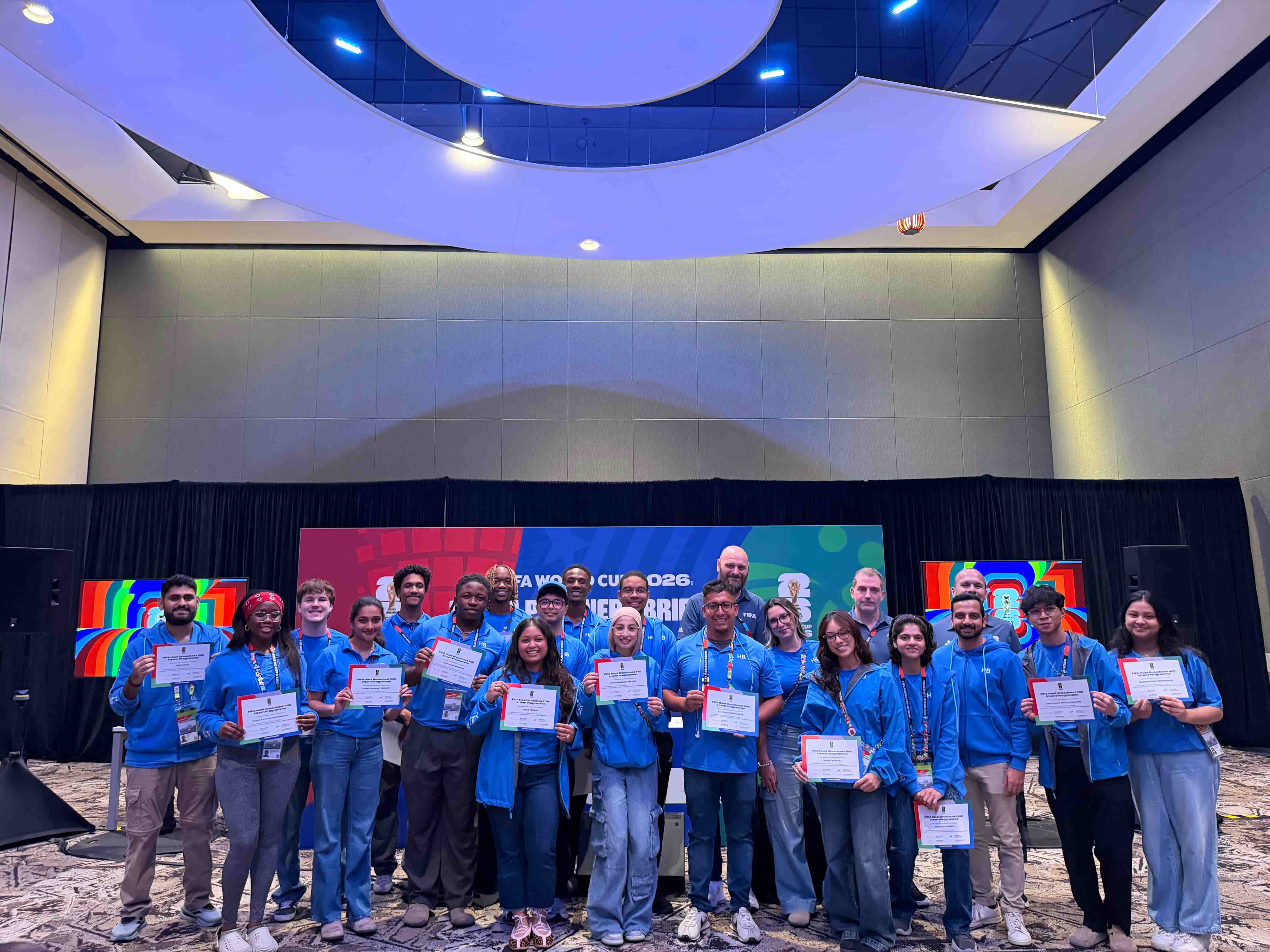 A group of interns in blue polos holding up certificates