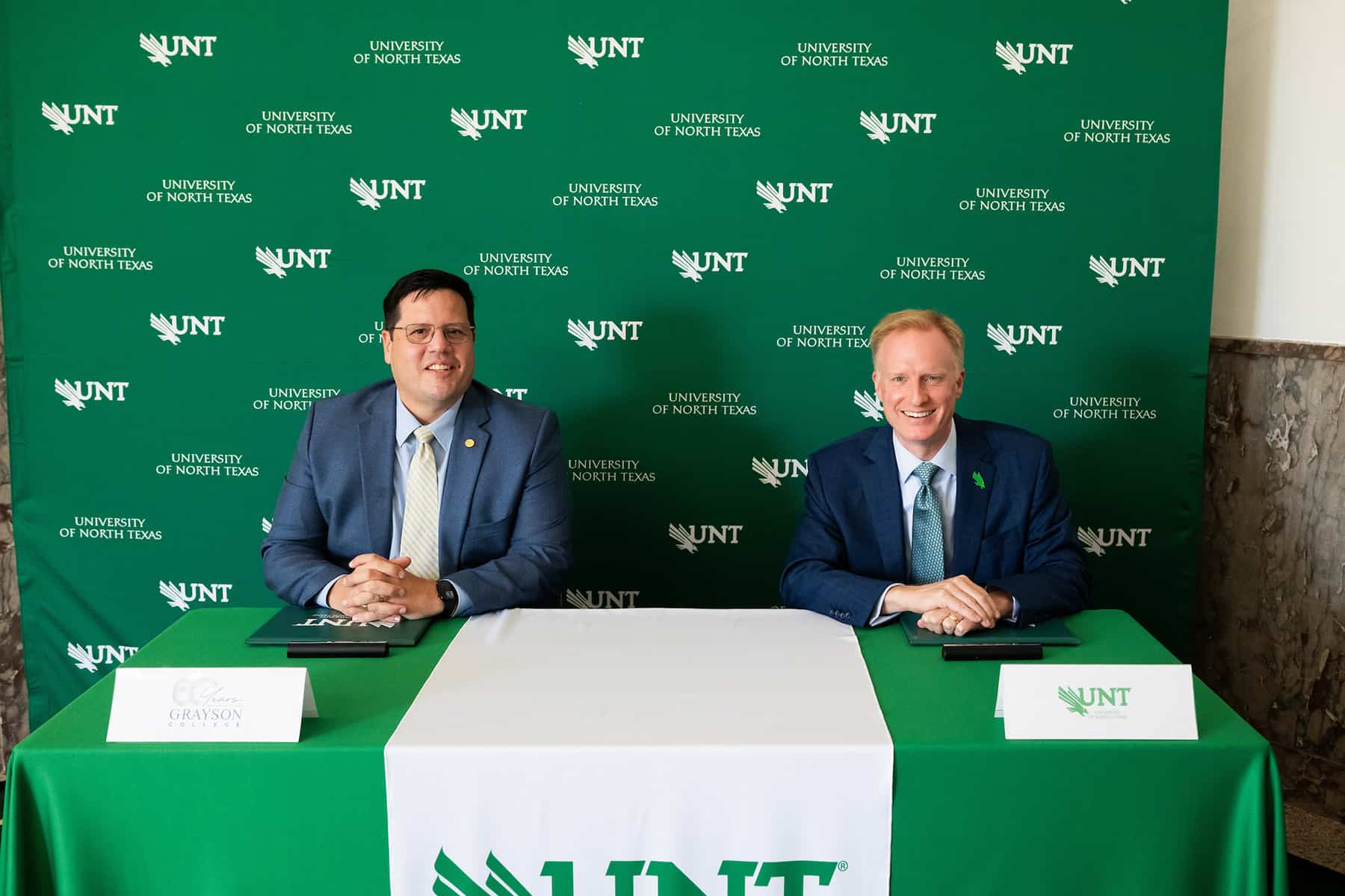 Grayson College president Jeremy McMillen and UNT president Harrison Keller sit at a table to sign a memorandum of understanding