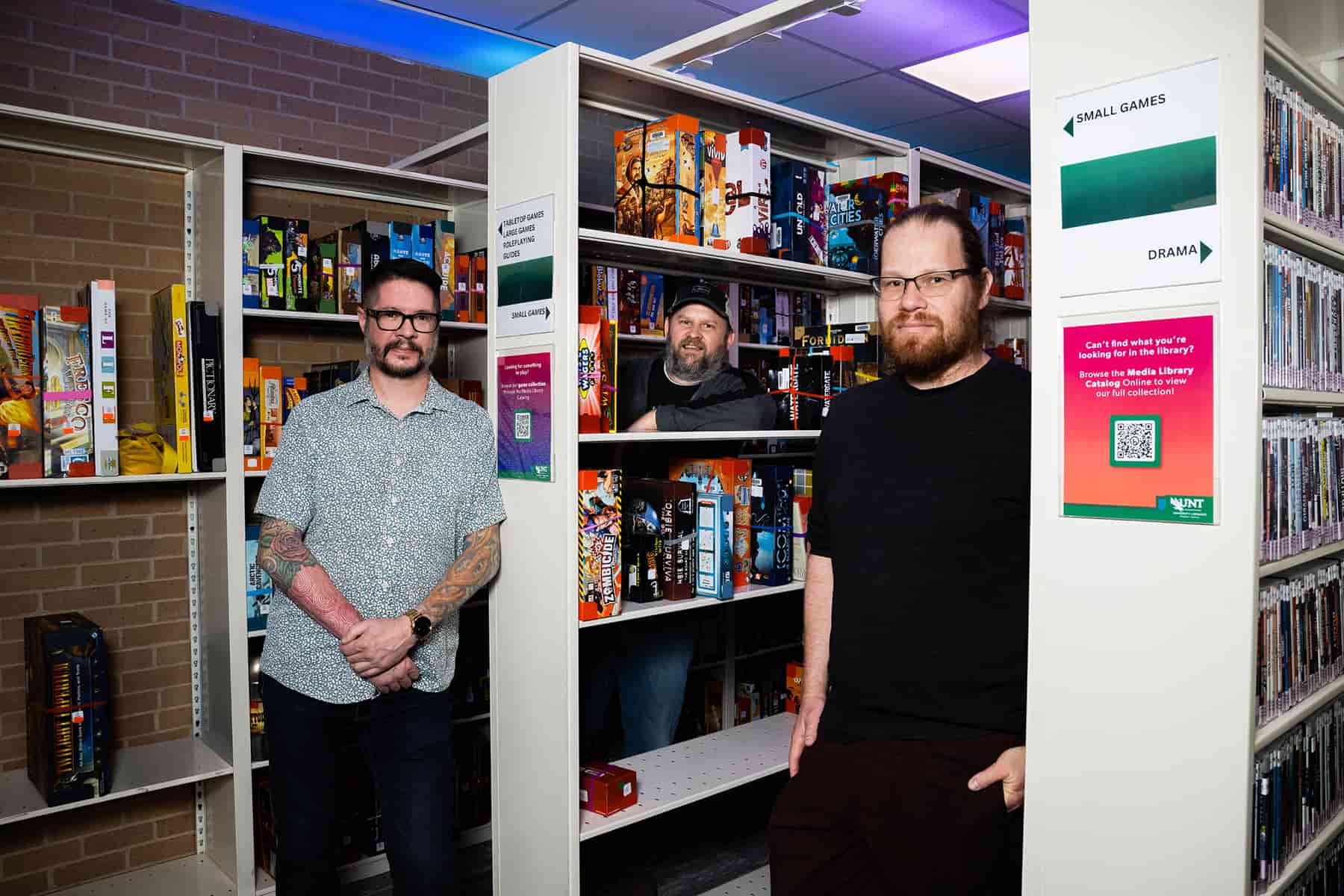 Three professors stand between shelves of video games in a library