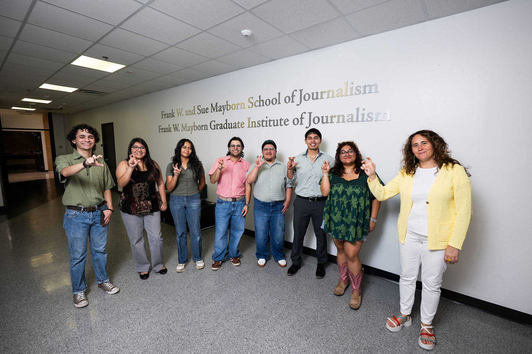 A group of seven students and their professor stand in front of a white wall, smiling