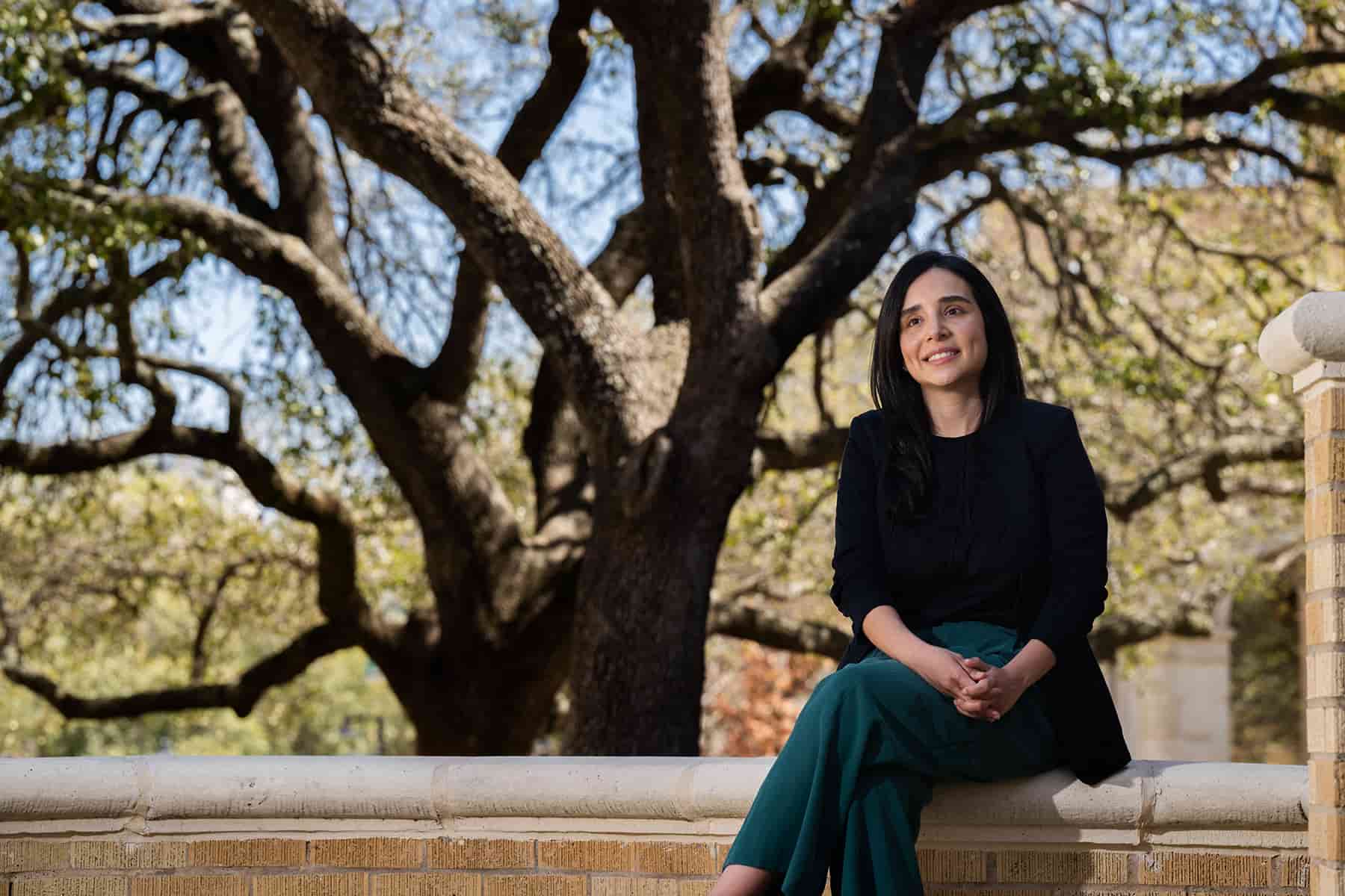 Isamar Almeida sits outside on a brick ledge in front of large trees