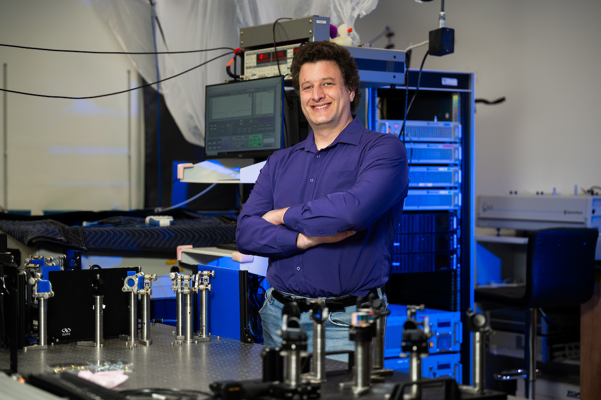 Jens Neu stands smiling in his lab. He wears a purple button down shirt and jeans.