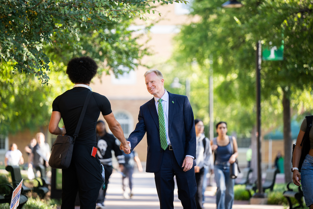 President Keller shakes hands with a male student, welcoming him back for the new semester