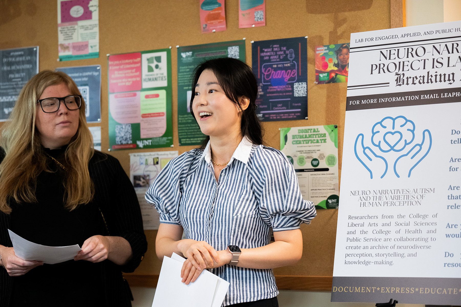 Two people stand next to a posterboard with information about a neuro-narratives project
