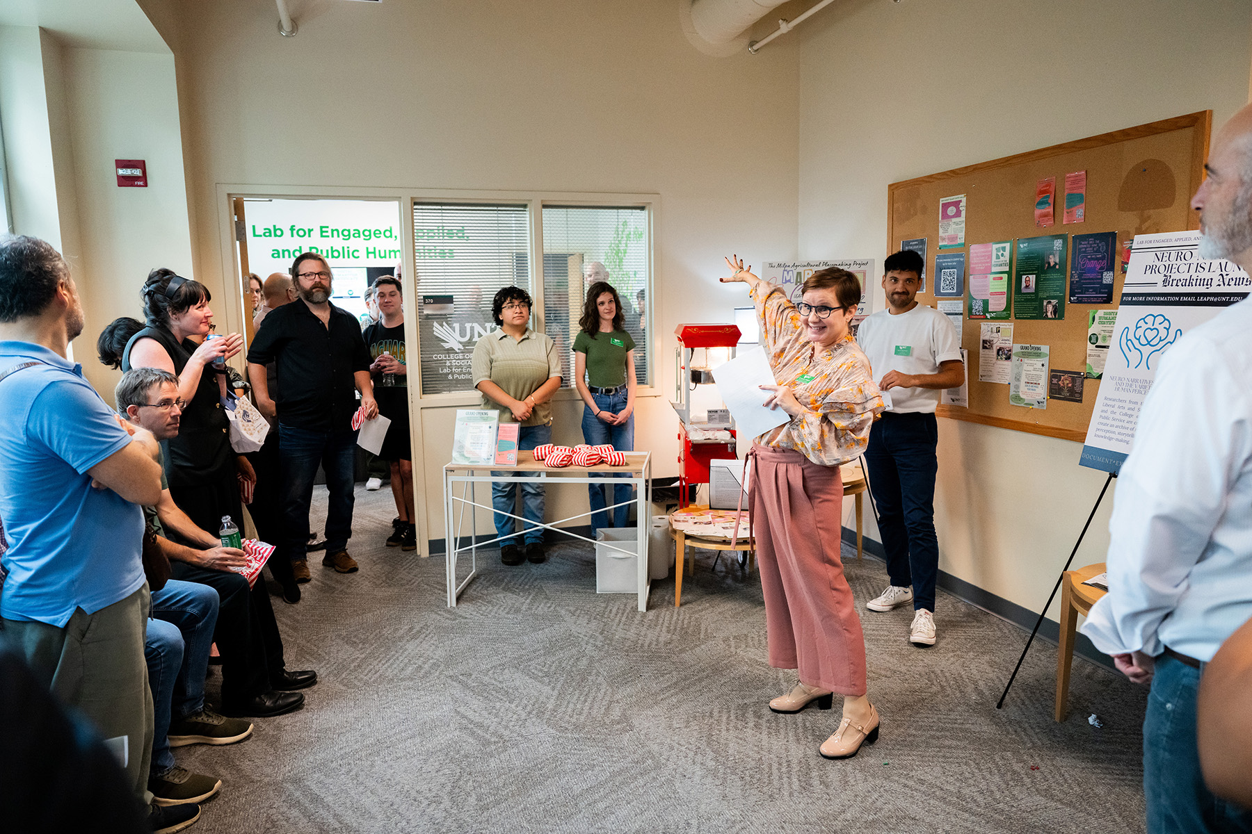 A person stands in front of a group of people and points toward a learning laboratory space. The crowd is gathered for the grand opening of this space.