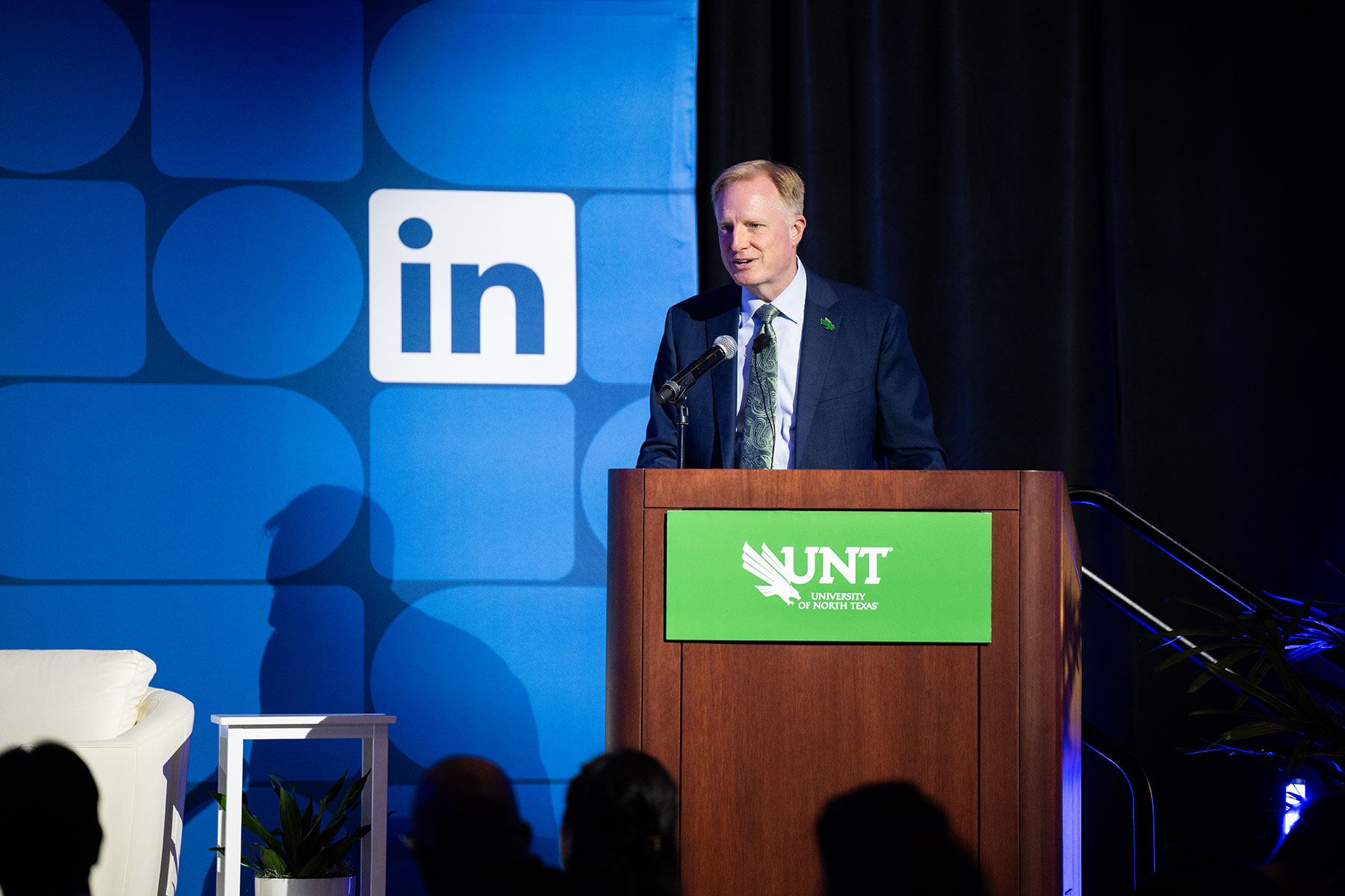UNT President Harrison Keller speaks at a wooden podium in front of a blue background