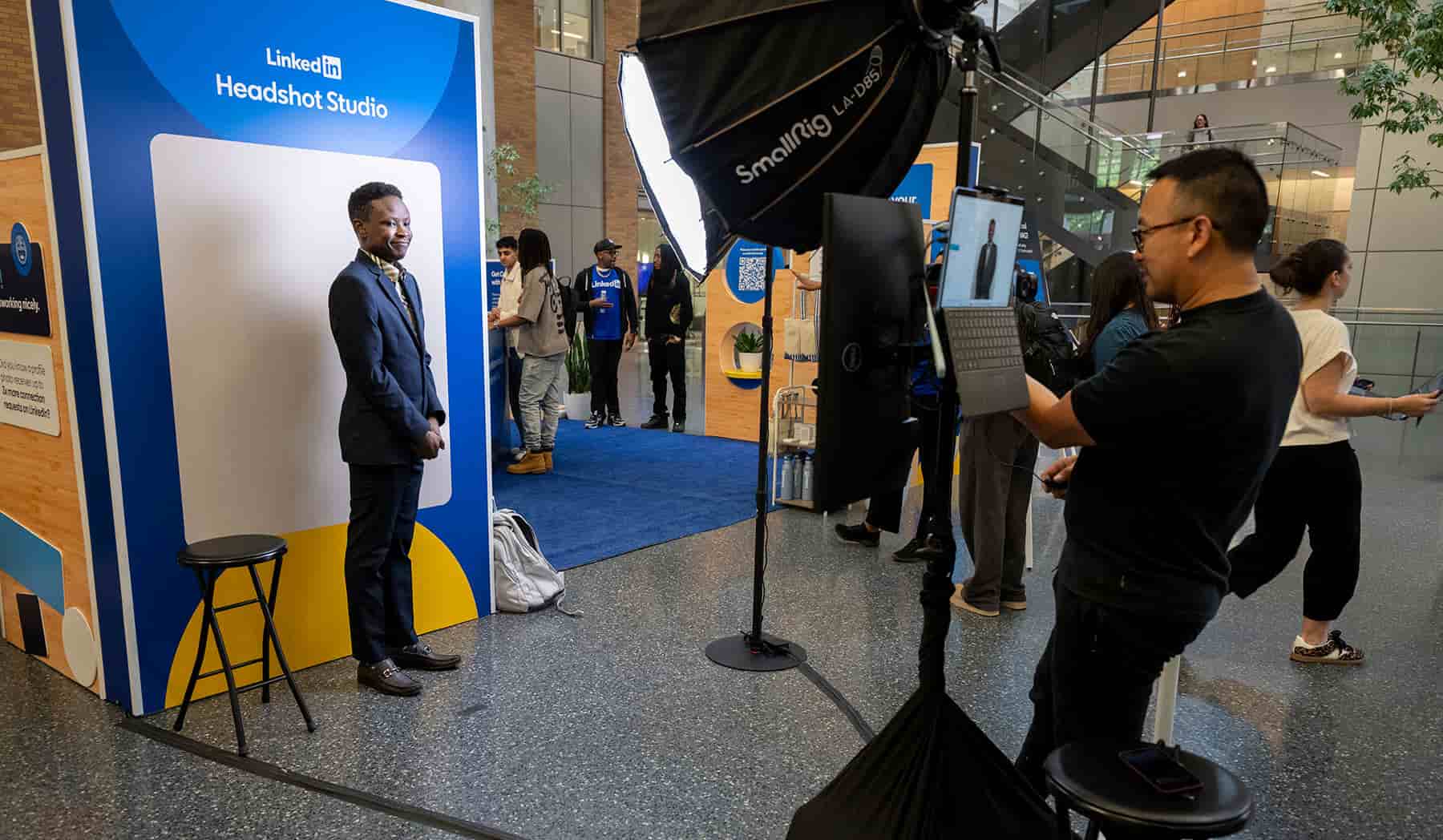 A smiling student stands in front of a backdrop while a photographer takes their picture