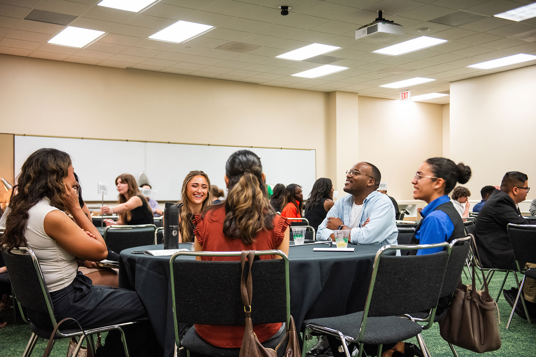 A mentor and students sit at a round table smiling and talking
