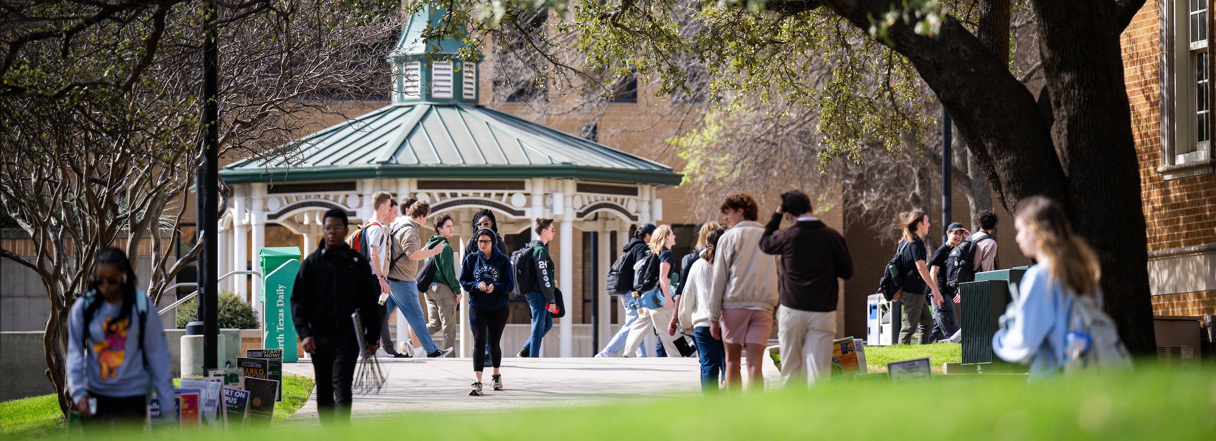 A shot of students walking on campus, a green and white gazebo stands in the background