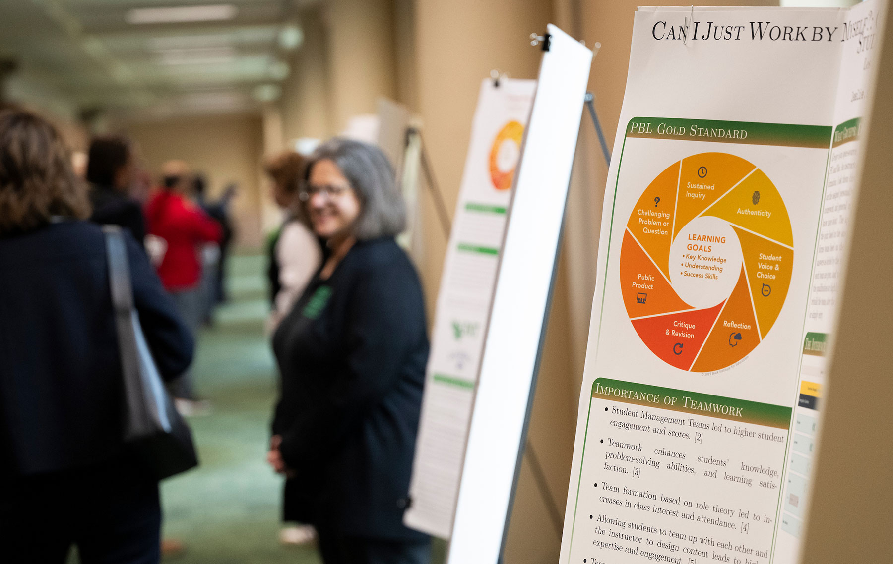 A poster with information about project-based learning is displayed in a hallway full of people