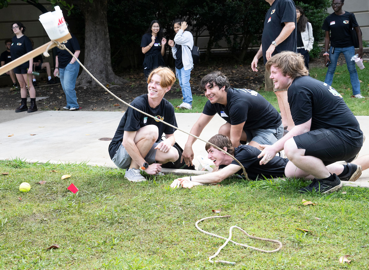 Four high school boys look off screen at a catapult that just fired. One is on the ground excitedly yelling