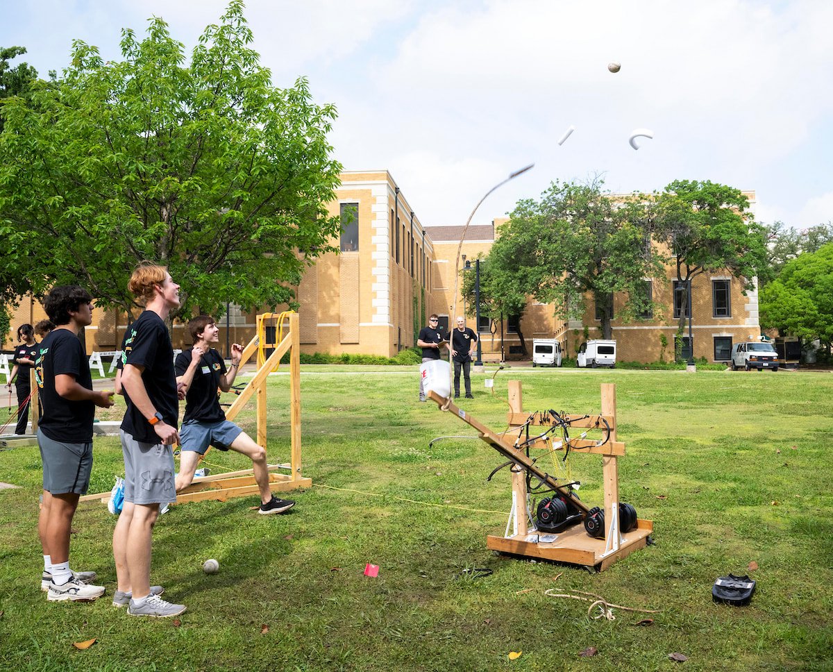 A student cheers after a catapult launch, two others watch