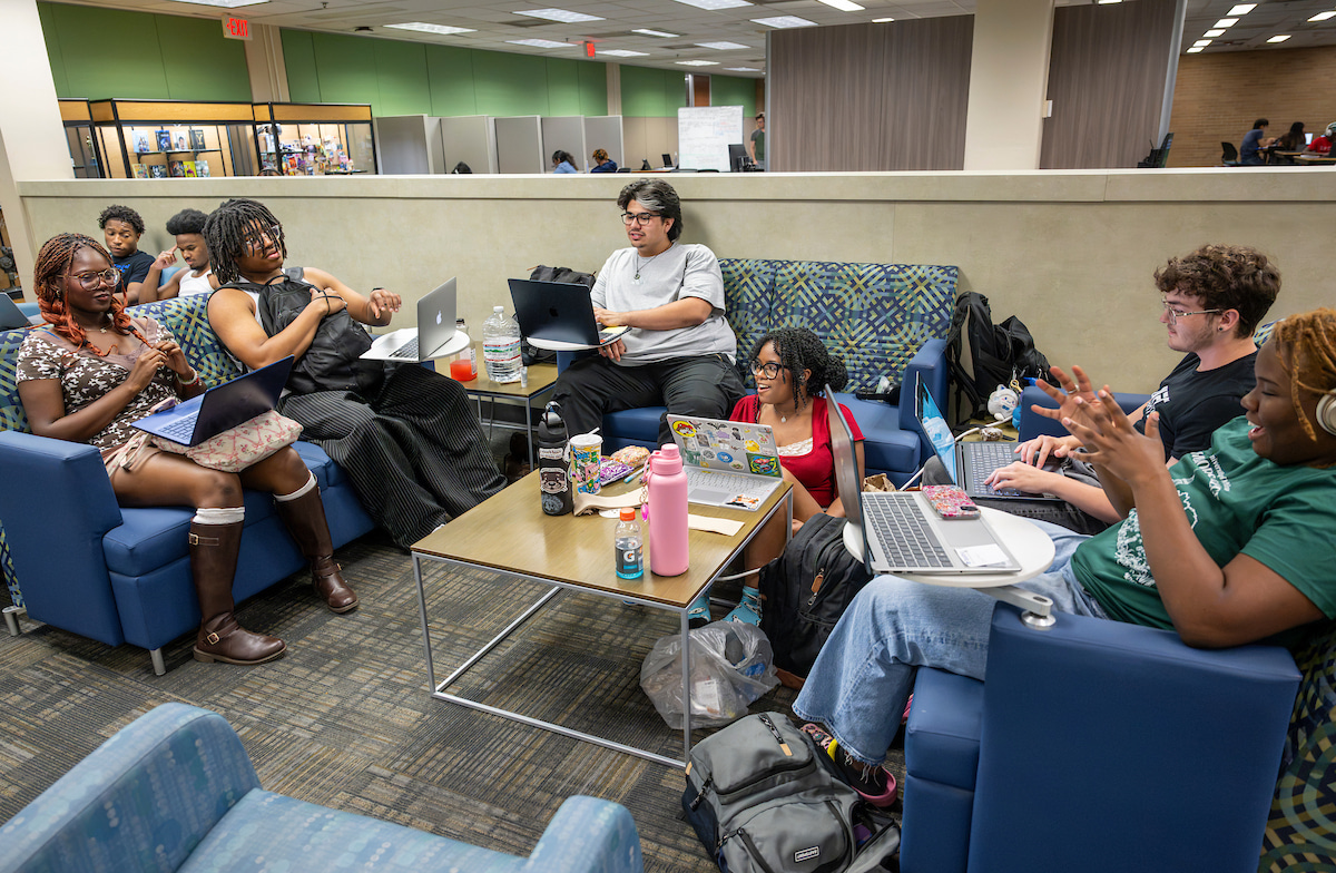 A group of student sit in a library lounge area chatting and laughing.