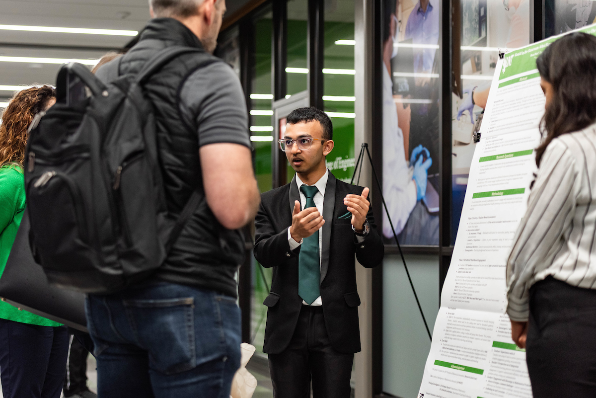A student standing in front of a research poster explaining his work to others