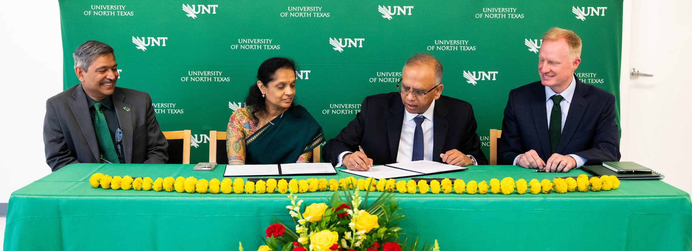 Dean Kinshuk, Anuradha, Vikas Sinha, and President Keller sit side by side at a green table