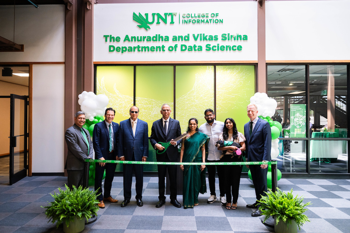 Eight people, including the Sinhas, stand behind a a green ribbon ready to open the The Sinha Innovation Lab for Data Science