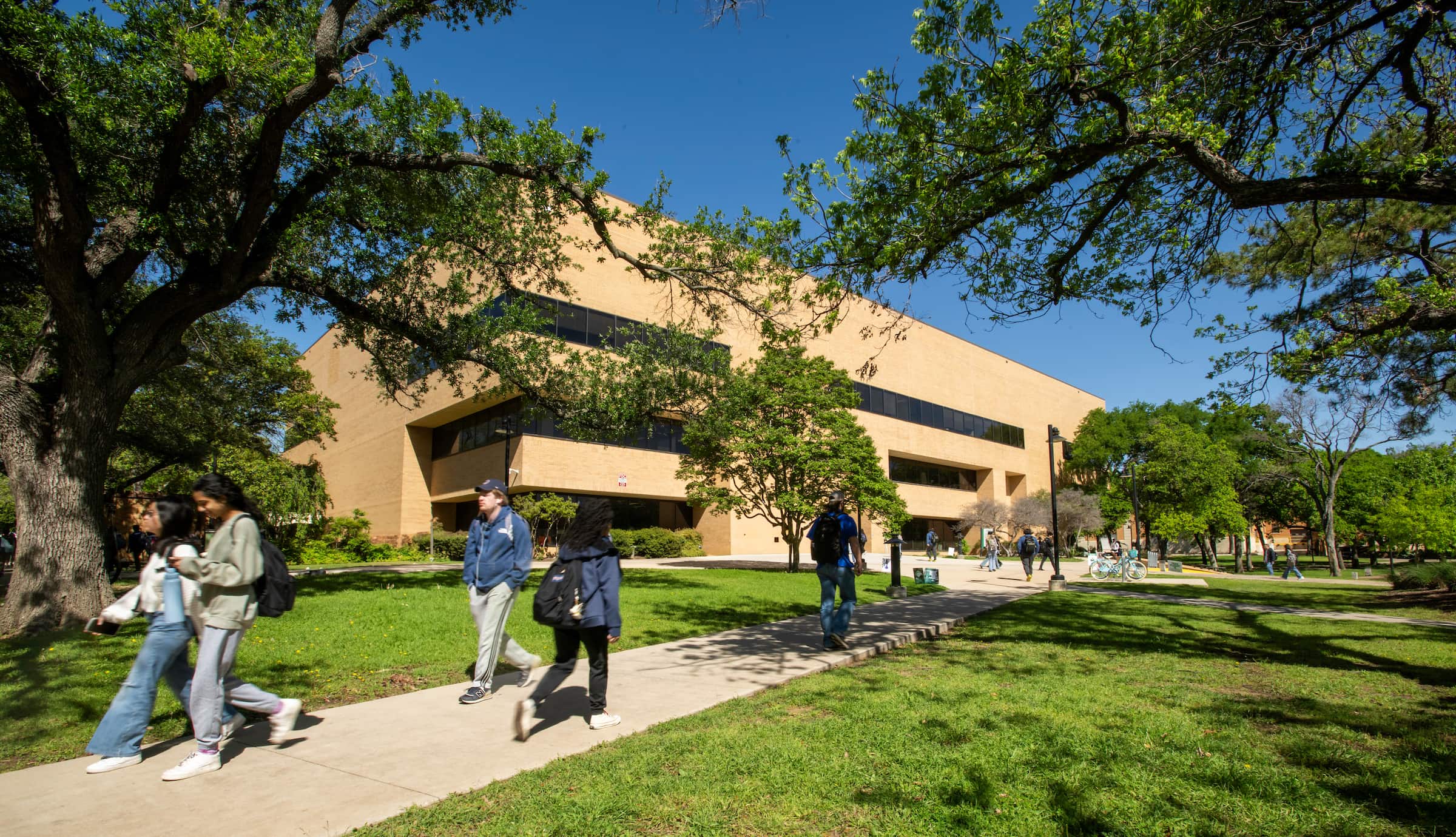 Various students walk on the sidewalk in front of the brick GAB building.