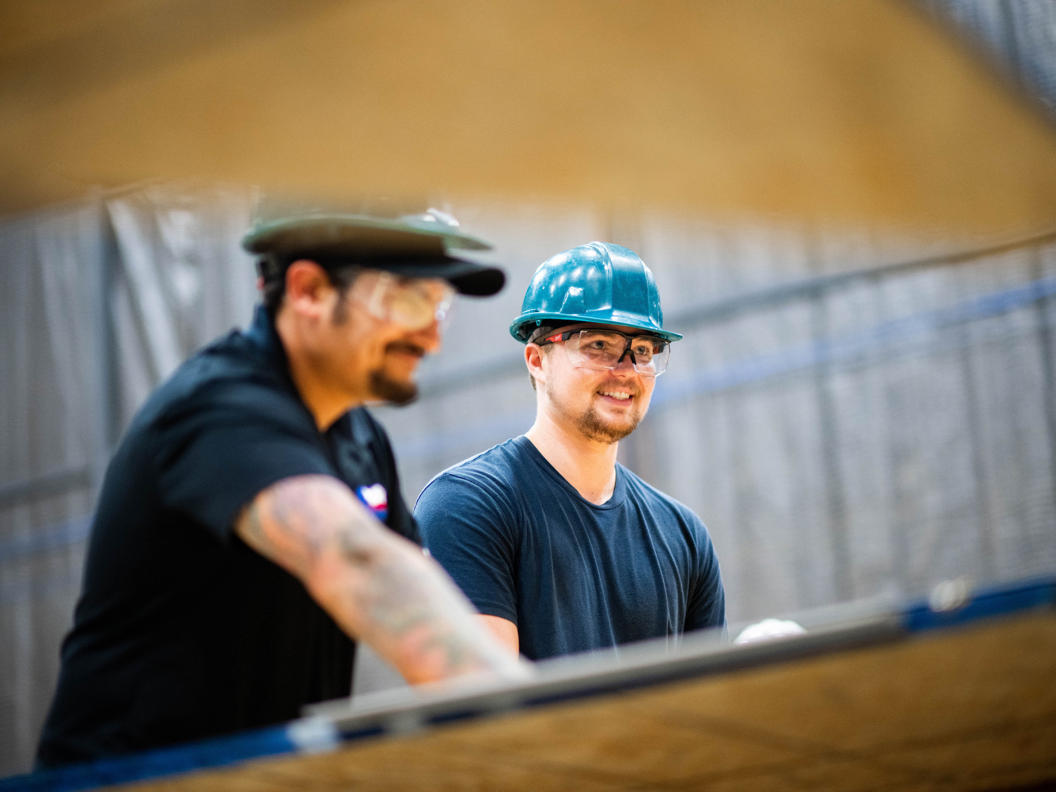 Two students in hard hats framed by plywood