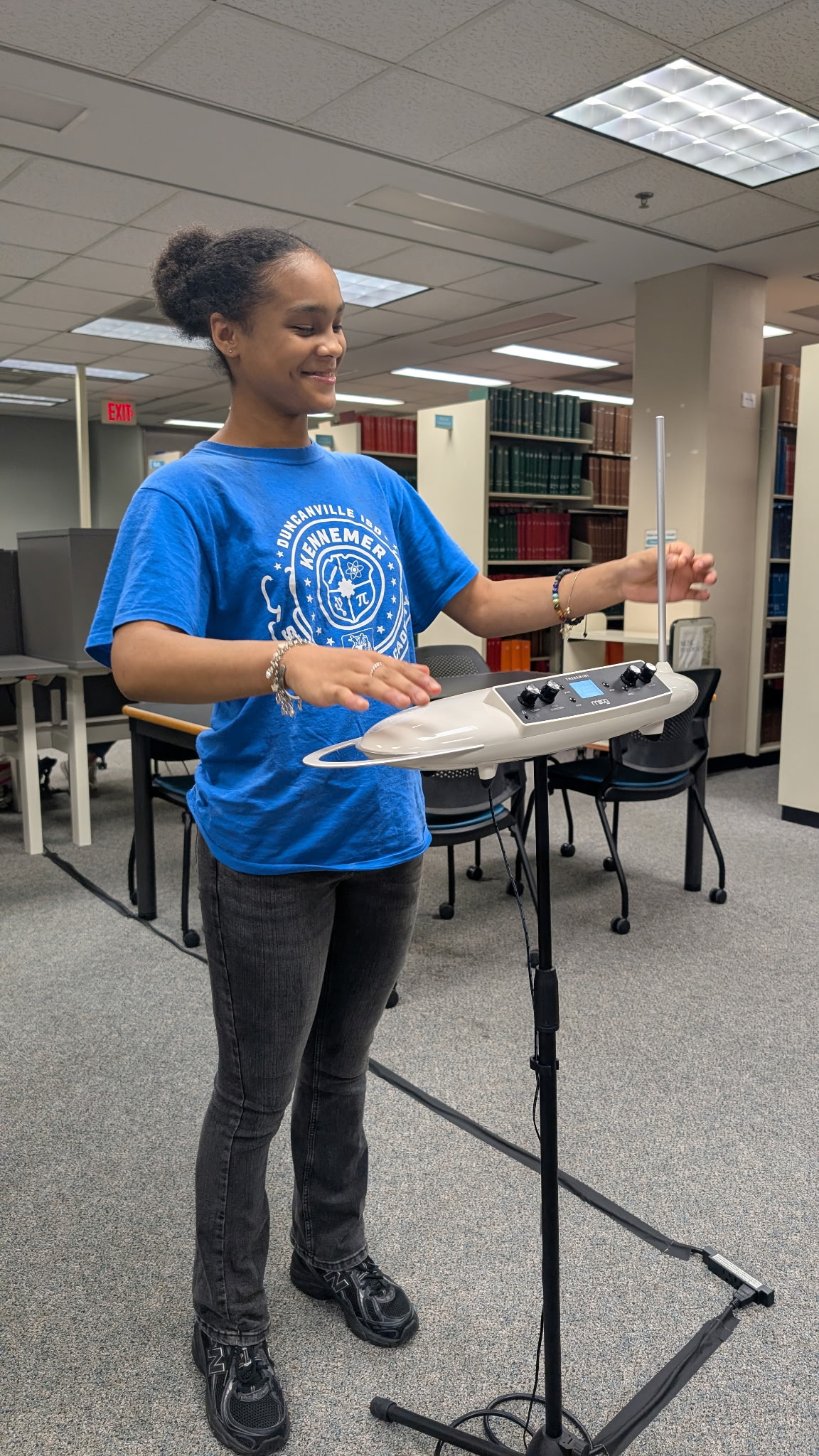 A female middle school student in a blue shirt waves her hand over a machine to make music