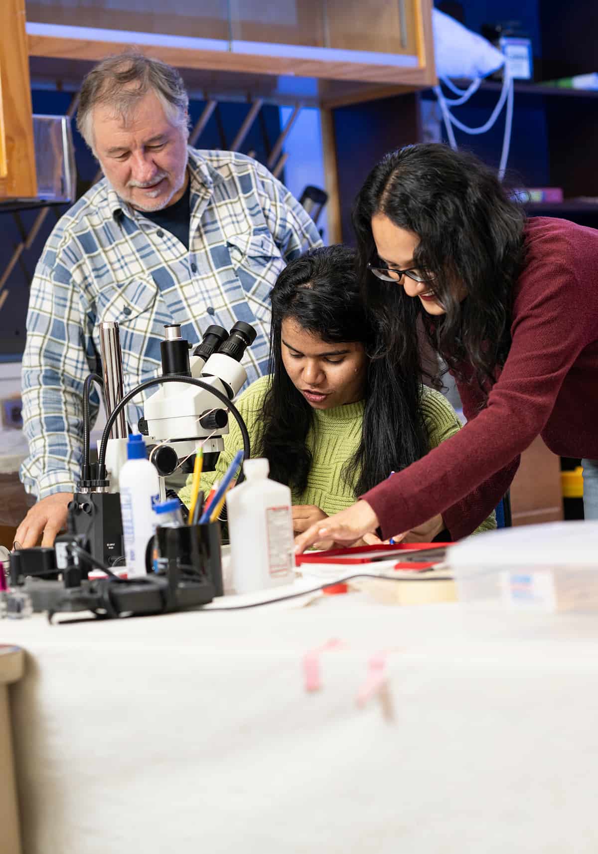 Three researchers study moss and lichen samples under a microscope