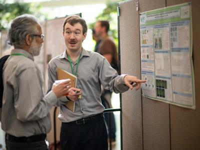 A UNT student presents his research poster to an onlooker