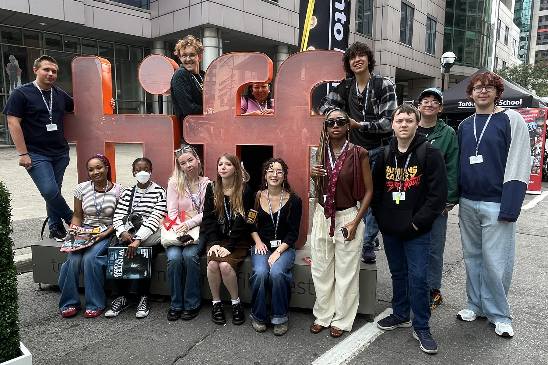 A group of students sit and stand by a red TIFF sign