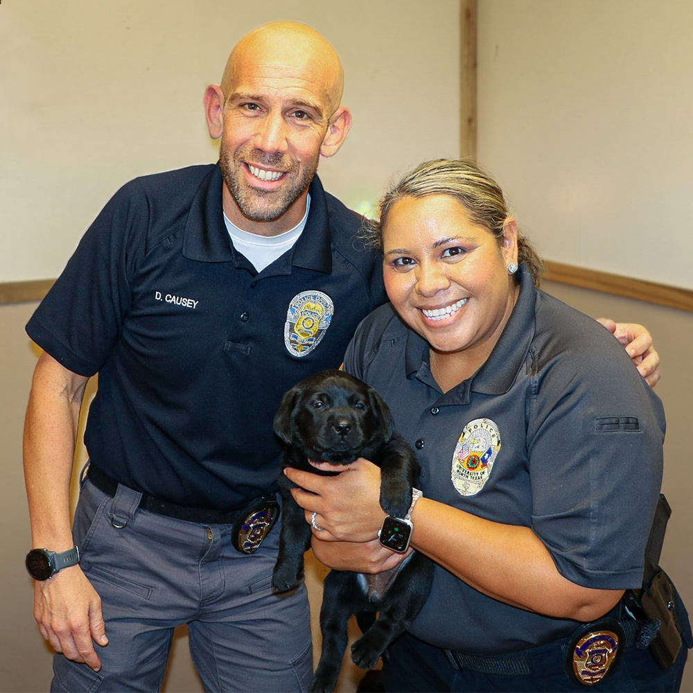 Two UNT police officers with an adorable black lab puppy