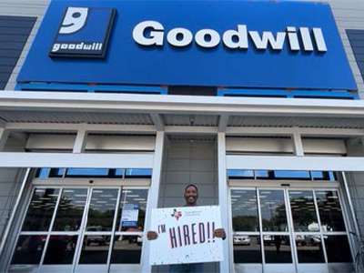 A WISE participant hold up an "I'm hired!" sign in front of a Goodwill storefront