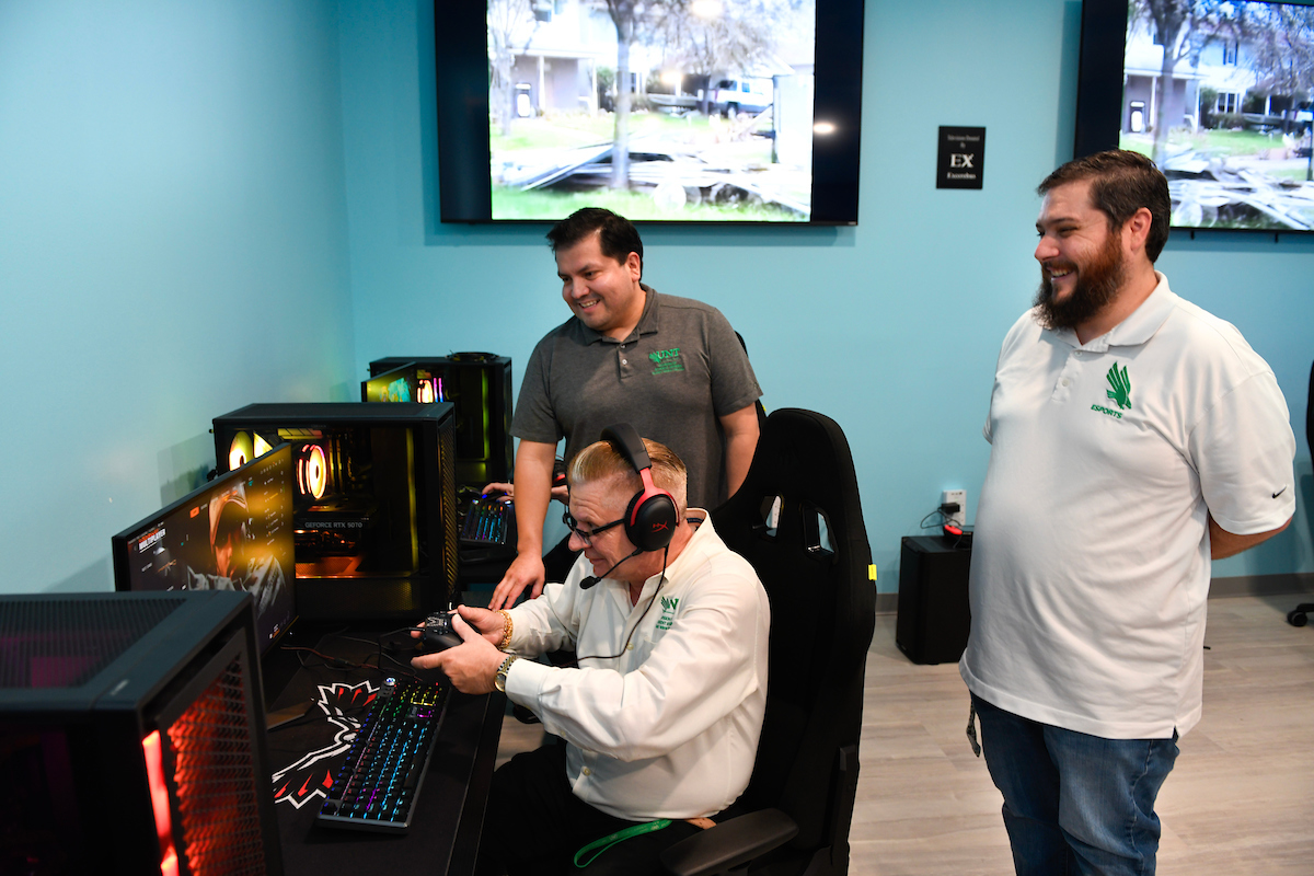A man plays on a computer as two others looks on and laugh happily