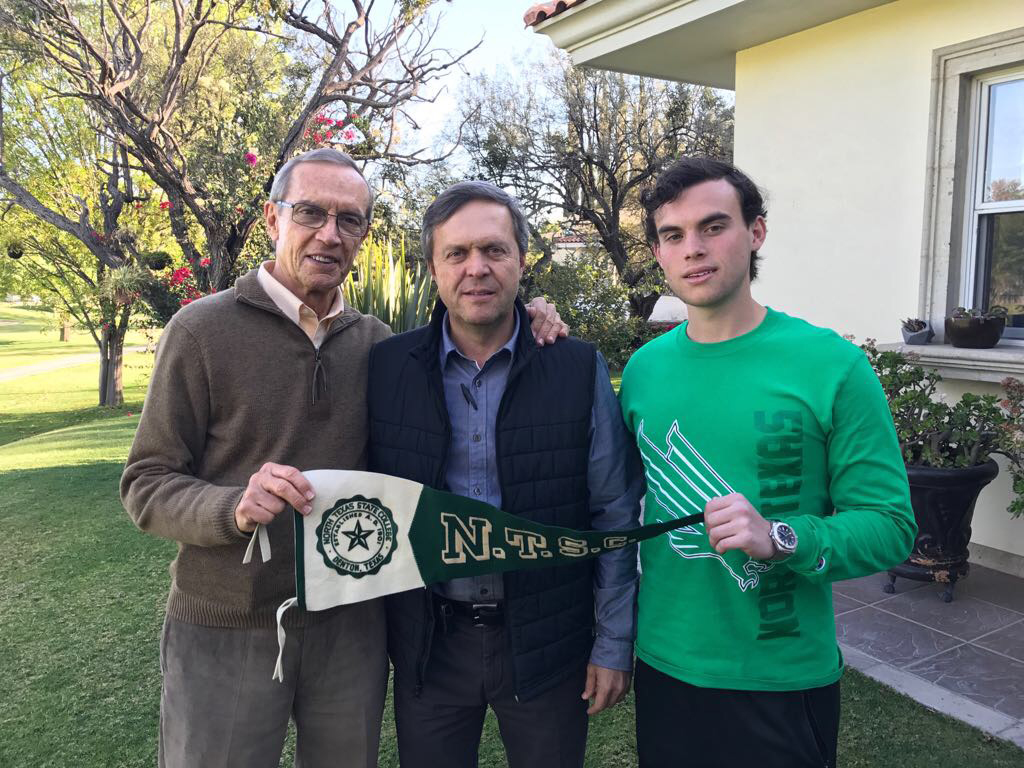 Three members of the Usabiaga family -- a grandfather, a father and a son -- stand holding a pennant from North Texas State University (UNT's one time name). From left to right: Ernesto G. Usabiaga, a 1959 UNT alumnus; Jorge Ernesto Usabiaga, a 1986 UNT alumnus; and Ernesto B. Usabiaga, a current UNT student. 